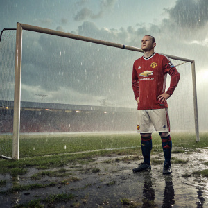 Wayne Rooney, wearing Manchester United jersey, standing on a rain-soaked football field.