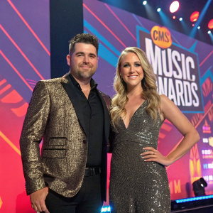 Josh Gracin and Katie Weir at Country Music Awards, glamorous attire, vibrant stage backdrop.