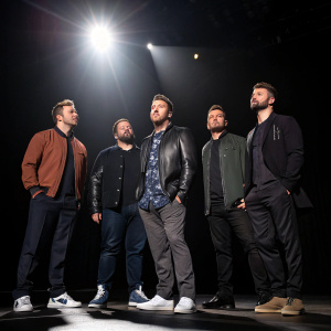 NSYNC members JC Chasez, Lance Bass, Joey Fatone, Chris Kirkpatrick, and Justin Timberlake. Attending a press conference. Dark stage with bright spotlight on them