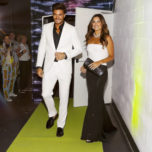 Mariano Di Vaio and Eleonora Brunacci on the red carpet. Flashy neon lights and crowd visible in the background