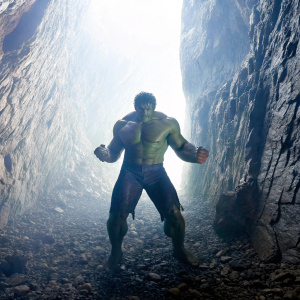 The Incredible Hulk flexing in a dimly lit, rocky cave. Emphasis on his massive size and strength through dramatic lighting and shadows.