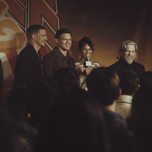 Channing Tatum, Halle Berry, Pedro Pascal, and Jeff Bridges at a bustling press conference. Behind them, vibrant, animated backdrop featuring bold, colorful logos and graphics. A crowd of excited fans and reporters in the foreground.
