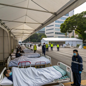 Outside Caritas Medical Center in Hong Kong, a makeshift tent with rows of hospital beds. Patients are wrapped in thermal blankets. Medical staff are on duty. The scene is calm and quiet.
