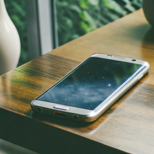 Samsung Galaxy S7 Edge, in space-themed wallpaper, on a sleek wooden table