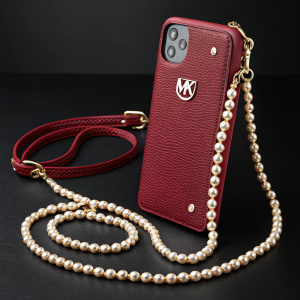 High-end iPhone case by Michael Kors. Rich red leather with embossed logo. Adorned with pearls and structured strap. Shot against sleek black backdrop