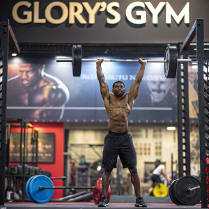 Promotional billboard for Glory's Gym. Muscular athlete lifting weights. Background showcases gym equipment and motivational quotes.