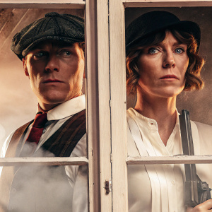Promotional poster for Peaky Blinders featuring main characters Tommy Shelby and Ada Shelby. Dark and moody atmosphere with vintage aesthetic. Serious and determined expressions. Dark color palette of grays and blacks. Period-appropriate clothing from early 20th century. Historical drama and crime setting. Promotional photograph style.