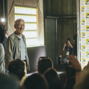 Sir Ian McKellen, at Comic-Con, in casual attire, with a friendly smile. Crowd in background