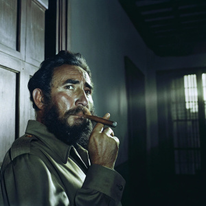 Close-up of Fidel Castro's face. The Cuban leader is smoking a cigar. Dimly lit room, shadows
