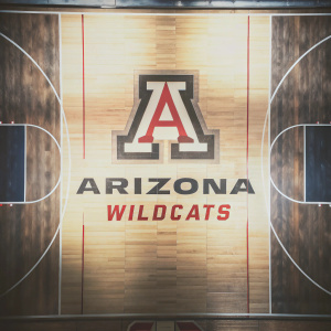 Arizona Wildcats basketball court, dark blue backdrop. Large 'A' logo with depth design. Sponsor and team logos strategically placed. Stylized graphic design of a basketball court.