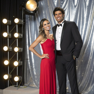 Mark Philippoussis and Silvana Lovin at a glamorous award show. They are posing in front of a shiny, silver backdrop.