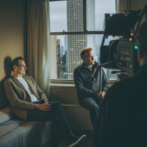 Conan O'Brien and Bob Saget, sitting on set with skyline view. Behind-the-scenes moment during taping of late night talk show