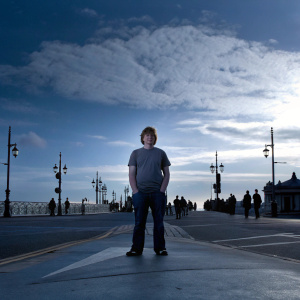 Rupert Grint in a casual t-shirt and jeans. Standing in a busy street. Bright daylight