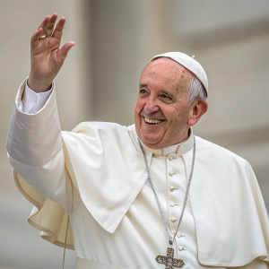 Close-up candid photo of Pope Francis. White papal robe and headpiece. Waving with a warm smile. Blurred, neutral-toned background.