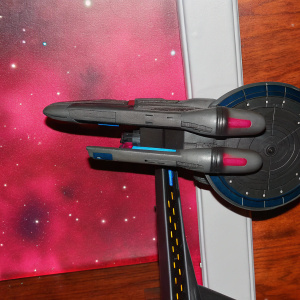 Digital illustration of the USS Rhode Island (NCC-72701) from Star Trek. Futuristic design with gray, blue, and red hues. Set against a starry cosmos backdrop, showcasing intricate ship details.