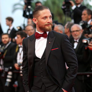 Tom Hardy, wearing a black tuxedo and red bowtie, at the Cannes Film Festival premiere. Crowds of photographers and fans in the background