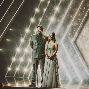 Ravi Kishan and Preeti Kishan at a formal awards ceremony. Bright stage lights, colorful backdrop