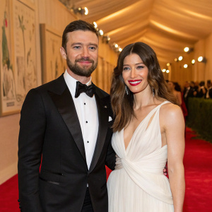 Justin Timberlake and Jessica Biel attend the Met Gala. Timberlake in a black tuxedo with a neatly trimmed beard. Biel, in a white, flowing gown, beams warmly. The venue is lavishly decorated with art pieces.