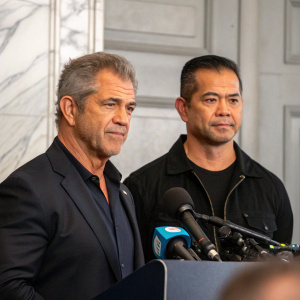 Mel Gibson and Rick Sarmiento at a press conference. Gray and white backdrop.