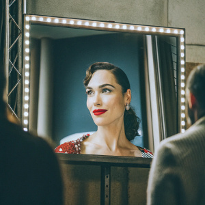 Gal Gadot, glamorous close-up. Elegant updo, red lipstick, sophisticated expression. Gray backdrop, professional lighting