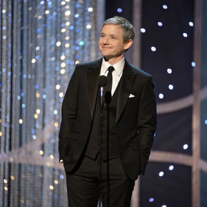 Martin Freeman at a glitzy awards show. Elegant black suit and tie, standing in front of a shimmering backdrop.