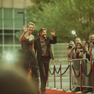 Charlize Theron and Joe Roth at a movie premiere. Red carpet, smiling. Surrounded by photographers and fans.