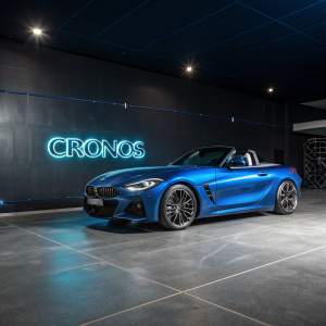 Blue BMW Z4 parked in a sleek, modern showroom. High gloss finish, highlighting the car's aerodynamic design. Dark background with neon text 'CRONOS' in Portuguese.