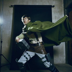 Cosplayer in Attack on Titan Recon Corps outfit. Dynamic pose on a plain white backdrop. Bright lighting, intense focus