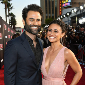 Adrian Bellani and Emmanuelle Chriqui attending a glamorous Hollywood movie premiere. They are dressed in designer outfits and are grinning widely.