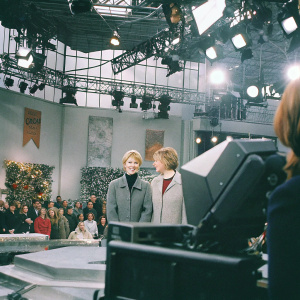 Anne Heche and Ellen DeGeneres on talk show set. Audience visible in background. Cheerful atmosphere. Bright lights and cameras present