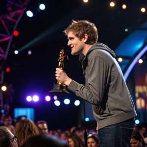Bo Burnham receiving an award. Golden statue, Film Independent Spirit Awards. Crowded stage, flashing lights