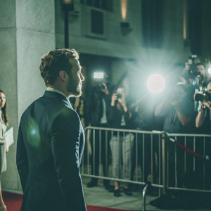 Jai Courtney, wearing a navy suit, attends the New York Film Festival. Crowded red carpet, flashing lights
