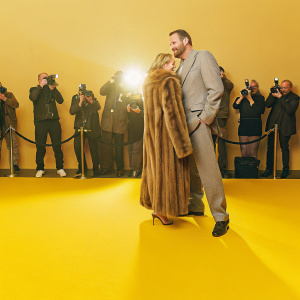 Joanne Mas and Danny Dyer, both on the red carpet. He is in a gray suit, she is in a long fur coat. Crowds of photographers and fans