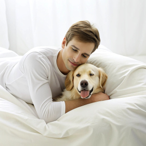 Young man and dog sleeping together in white bed at home