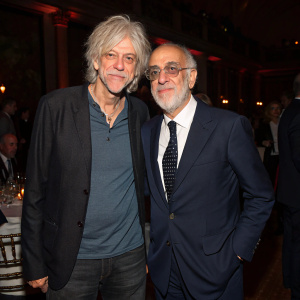 Bob Geldof and Alan Yentob at a charity gala. Bob in casual attire, Alan in formal suit. Dimly lit room with guests.