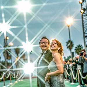 Michael Emerson and Carrie Preston attending a glitzy Hollywood awards ceremony. Background filled with flashing lights and excited crowd.