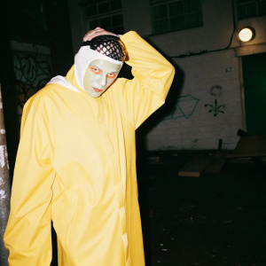 Mojo Jojo from Powerpuff Girls, green face with red eyes, wearing a spiked headband. Dark alleyway background with graffiti