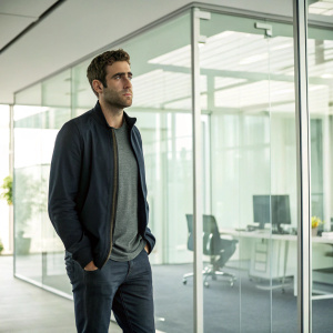 Oliver Jackson-Cohen as Jonathan Harker in modern-day office setting. Brightly lit room, glass walls, casual attire.