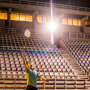 Lee Chong Wei, Malaysian badminton player, striking a powerful pose with racket raised. Empty stadium, spotlight on him.