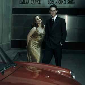 Emilia Clarke and Cory Michael Smith at an exclusive gala. Emilia in a stunning gold sequined dress. Cory in a classic black suit. They pose in front of a sleek, modern backdrop featuring the event sponsor's logo.