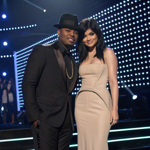 Ne-Yo in black suit, Kylie Jenner in beige gown. They pose on stage with bright LED backdrop. MTV Video Music Awards event.
