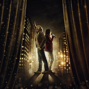 Natalie Casey and Ian H Watkins performing on Broadway. They are on stage in 'Fame: The Musical'. The backdrop features bright city lights.