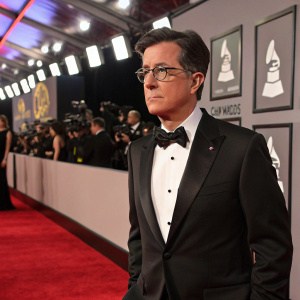 Stephen Colbert, dressed in a tuxedo, on the red carpet of the Grammy Awards. Serious expression.