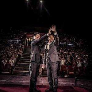 Andy Lau and Herman Yau Lai-To at a film festival. On stage with vibrant stage design. Audience visible in the background.