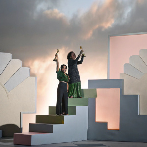 Anjana Vasan and Meera Syal, celebrating their Olivier Award win. Golden statues and vibrant stage design backdrop