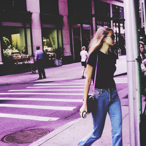 Rosie Huntington-Whiteley in casual attire. Jeans and black t-shirt. Walking through a busy city street, past shop windows and street vendors.