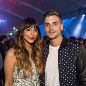 Hannah Simone and Jesse Giddings at an indoor music festival. Hannah has long wavy hair and a joyful expression. Jesse has short hair and a stylish outfit. They are standing close to each other in a crowded room with blurred guests in the background.