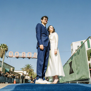 Zach Woods and Jocelyn DeBoer attending the premiere of 'Eighth Grade'. Zach in a sharp navy suit, Jocelyn in a sleek white dress. Hollywood Blvd backdrop