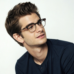 Andrew Garfield, with glasses and short hair, appearing in a candid photo shoot. Close-up portrait, studio setting