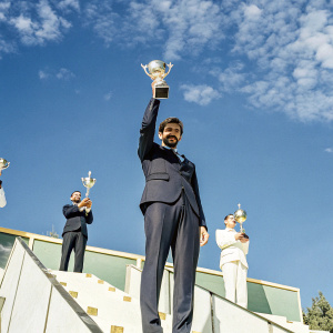 Michael Phelps at an award ceremony. Dressed in a black suit. Shiny trophies and other athletes in the background